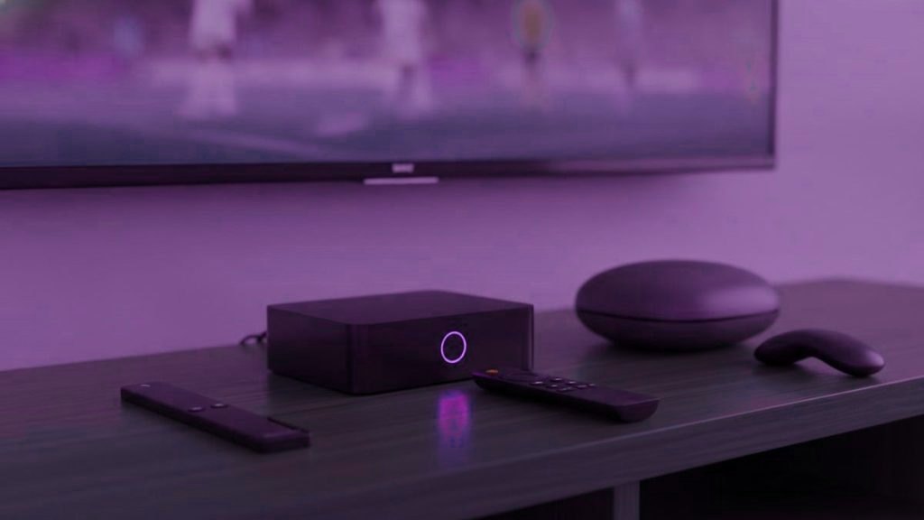 A streaming stick, a set-top box and a round streaming box with their remotes on a TV console